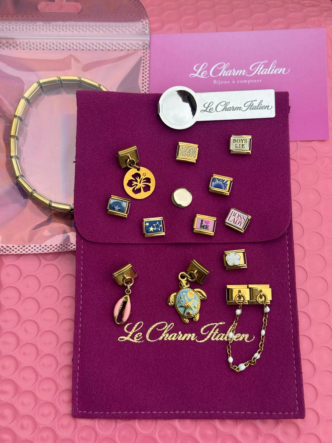 Pochette à bijoux fuchsia Le Charm Italien ouverte avec des charms italiens dorés et un bracelet posés dessus
